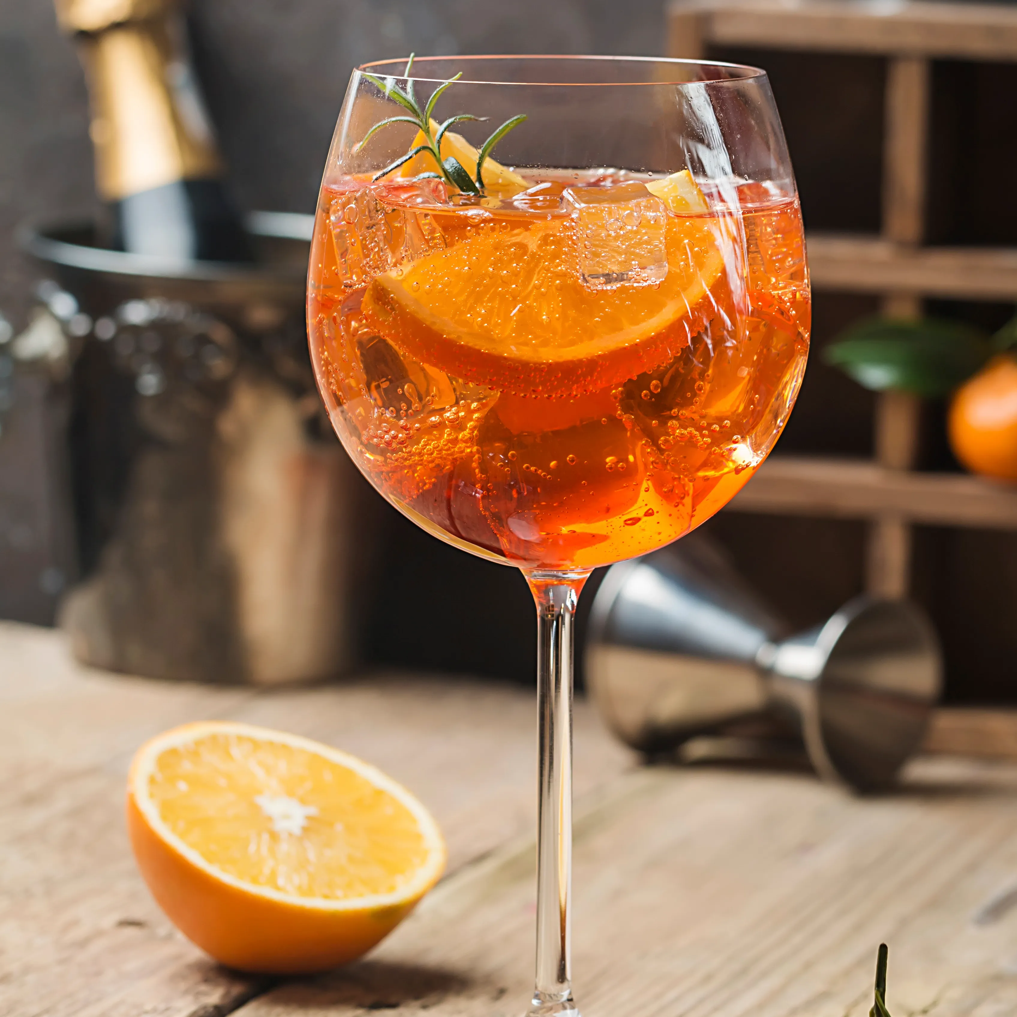 Calice di Aperol Spritz con ghiaccio, fette d'arancia e rosmarino su un tavolo rustico.